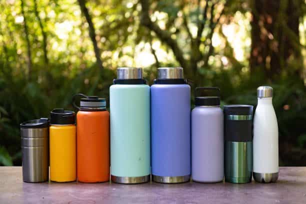 This is a color photograph of a variety of reusable water bottles on a picnic table outdoors during a summer family camping trip in California, USA.